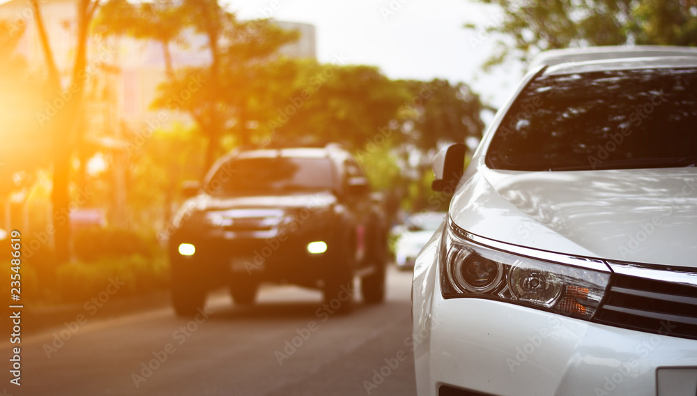Focusing on the White car headlights on a street corner with sunlight flares and small white car, In the background, the driver and car. Closeup headlights of car. Focusing on the White car headlights on a street corner with sunlight flares and small white car, In the background, the driver and car. Closeup headlights of car.