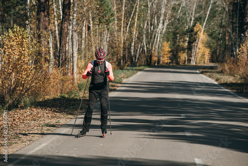 Training an athlete on the roller skaters. Biathlon ride on the roller skis with ski poles, in the helmet. Autumn workout. Roller sport. Adult man riding on skates. © ivandanru