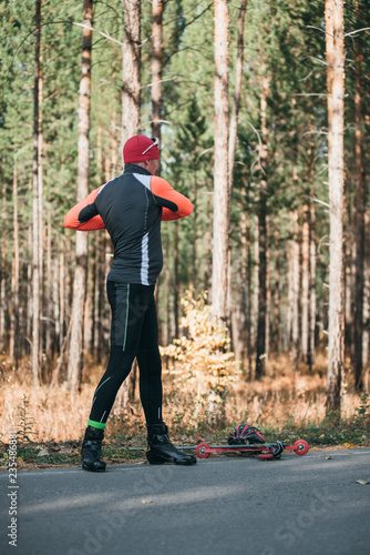 Training an athlete on the roller skaters. Biathlon ride on the roller skis with ski poles, in the helmet. Autumn workout. Roller sport. Adult man riding on skates. The athlete does the workout.