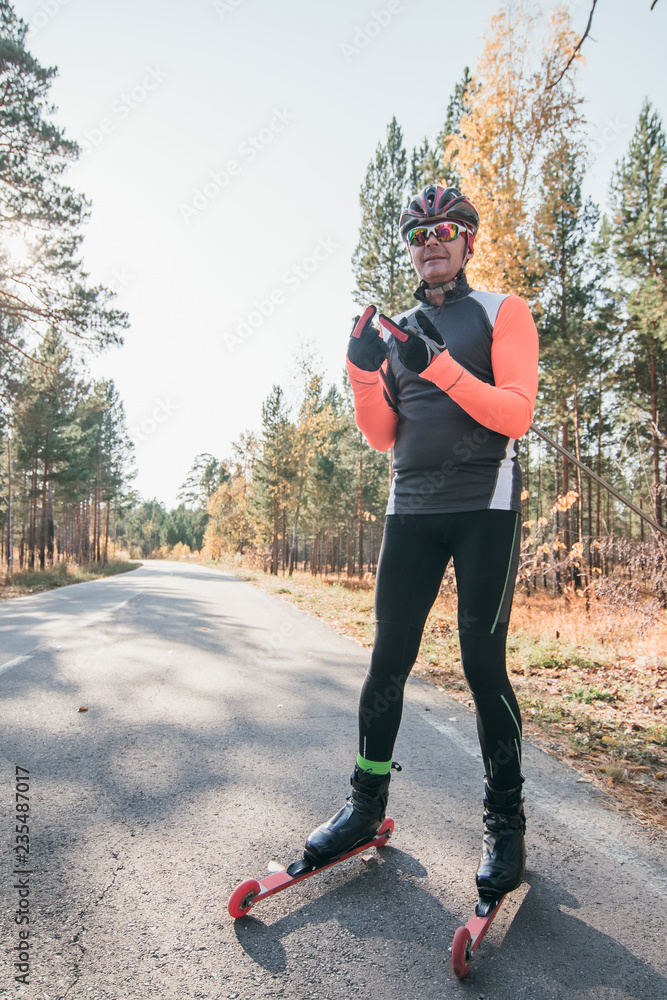 Training an athlete on the roller skaters. Biathlon ride on the roller skis  with ski poles, in the helmet. Autumn workout. Roller sport. Adult man  riding on skates. Stock Photo | Adobe