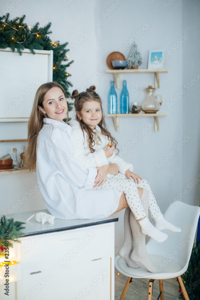 Baby girl in white and mother near Christmas tree
