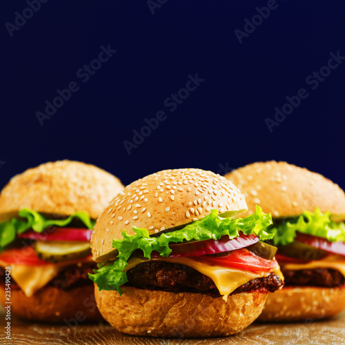 Three burgers with beef, tomato, pickled cucumber, cheese, onions and lettuce on wooden background. Tasty homemade food close up