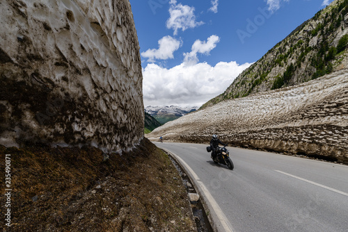 Motobiker rides through a turn of Nufenenpass pass road in spring inbetween the walls of snow, Switzerland photo