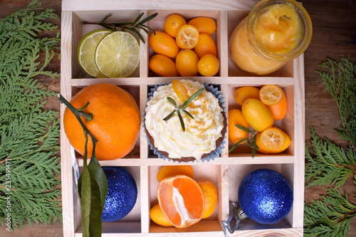 Cupcake garnished with butter cream  citrus curd  kumquats  mandarins  lime and Christmas balls in a wooden box with cells