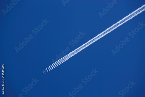 FOUR ENGINE JET AIRLINER WITH EXHAUST VAPOUR TRAILS IN CLEAR BLUE SKY