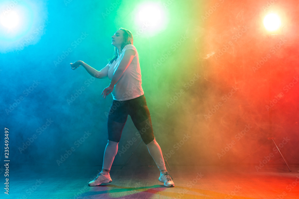 Dance, sport, and people concept - young woman dancing in the darkness under colourful light