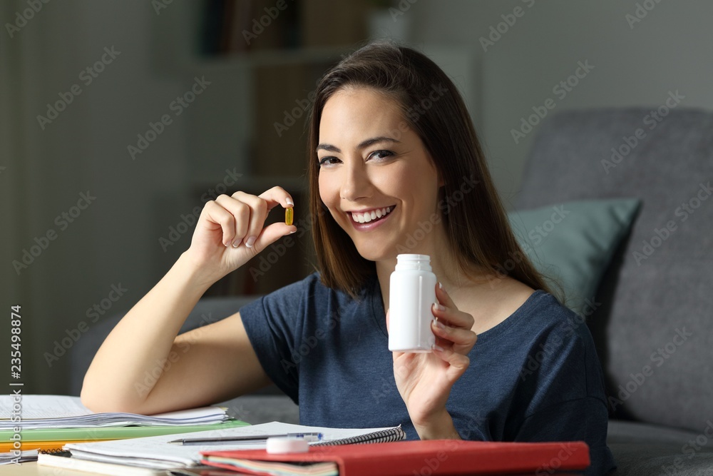 Happy student holding a vitamin pill studying in the night Happy student holding a vitamin pill studying in the night