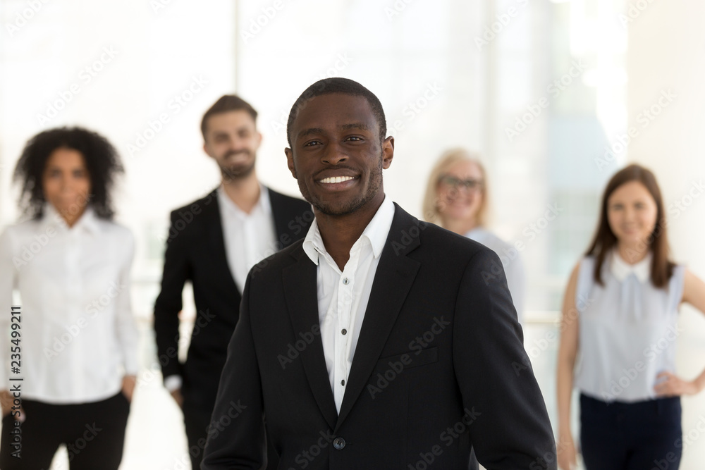 Portrait of smiling confident african american corporate leader or company ceo in suit posing with diverse team, happy professional black business coach, successful male executive looking at camera Portrait of smiling confident african american corporate leader or company ceo in suit posing with diverse team, happy professional black business coach, successful male executive looking at camera