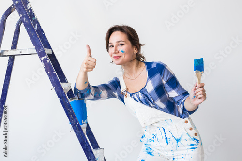 Repair  renovation  worker and people concept - Happy young woman paint wall at home  showing us thumbs up