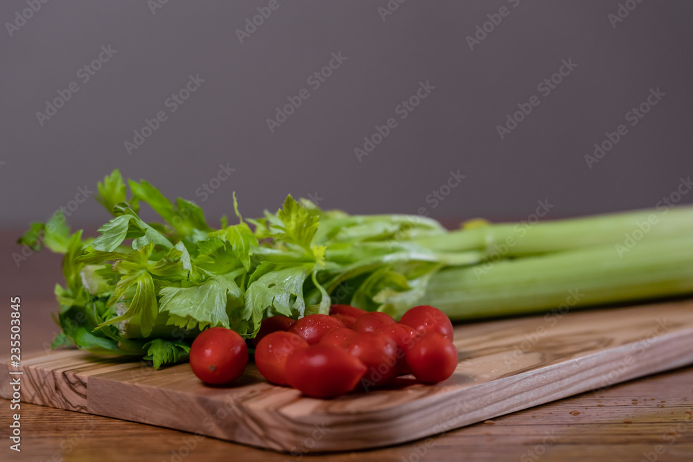 Fresh celery and tomatoes on a cutting board on a rustic wooden table Fresh celery and tomatoes on a cutting board on a rustic wooden table