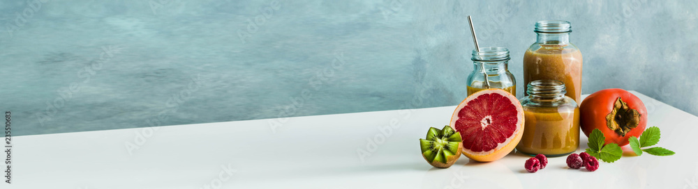 different glasses with freshly made grapefruit, kiwi, persimmon and raspberry smoothies. on white table and blue background. healthy food. morning breakfast different glasses with freshly made grapefruit, kiwi, persimmon and raspberry smoothies. on white table and blue background. healthy food. morning breakfast