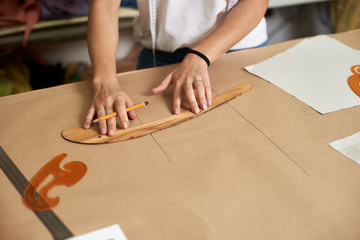 Working place in design studio. Female designer drawing flat paper patterns using measuring tape and curves on blurred background of tailor atelier interior. Exclusive clothes making concept.
