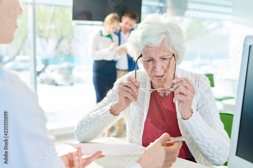 Obraz na plátně Serious confused senior lady with gray hair sitting at table and looking through