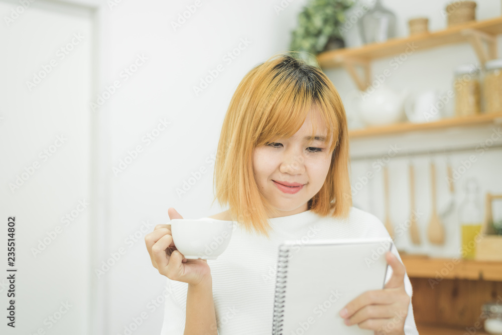 Asian woman write shopping lists in notepad by pen on her kitchen counter at home and reading and tries to remember all ingredients to shopping in grocery. Lifestyle women relax at home concept. Asian woman write shopping lists in notepad by pen on her kitchen counter at home and reading and tries to remember all ingredients to shopping in grocery. Lifestyle women relax at home concept.