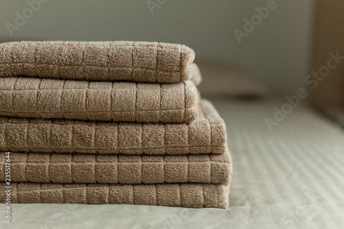 Stack of beige hotel towel on bed in bedroom interior.