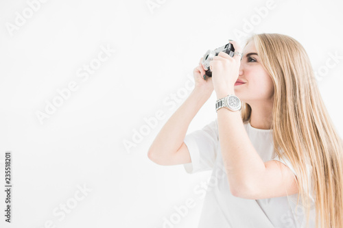 Portrait of a young stylish blonde girl using and taking pictures on an old vintage camera on a white background