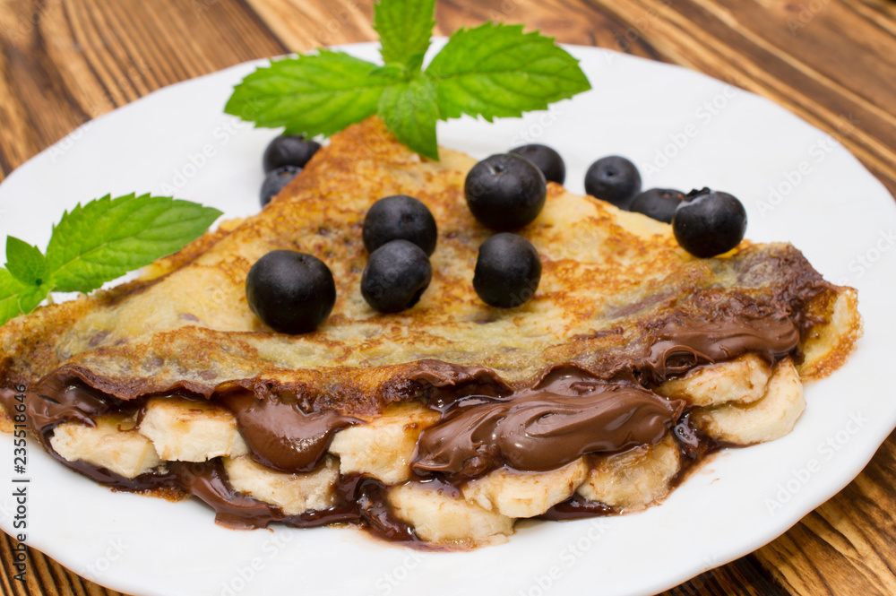 homemade crepes with chocolate cream, banana and blueberries on white background. pancakes