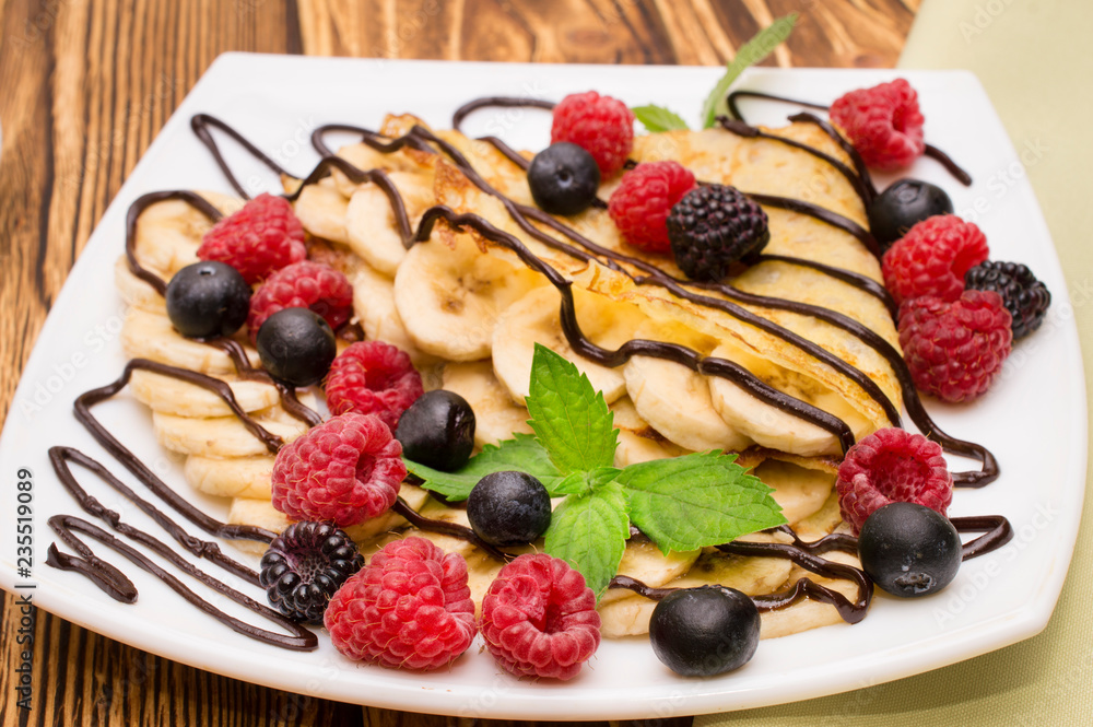 Homemade crepes served with chocolate cream, Banana, fresh blueberries, raspberries on a wooden background, pancakes Homemade crepes served with chocolate cream, Banana, fresh blueberries, raspberries on a wooden background, pancakes