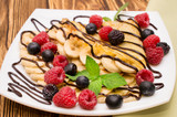 Homemade crepes served with chocolate cream, Banana, fresh blueberries, raspberries on a wooden background, pancakes