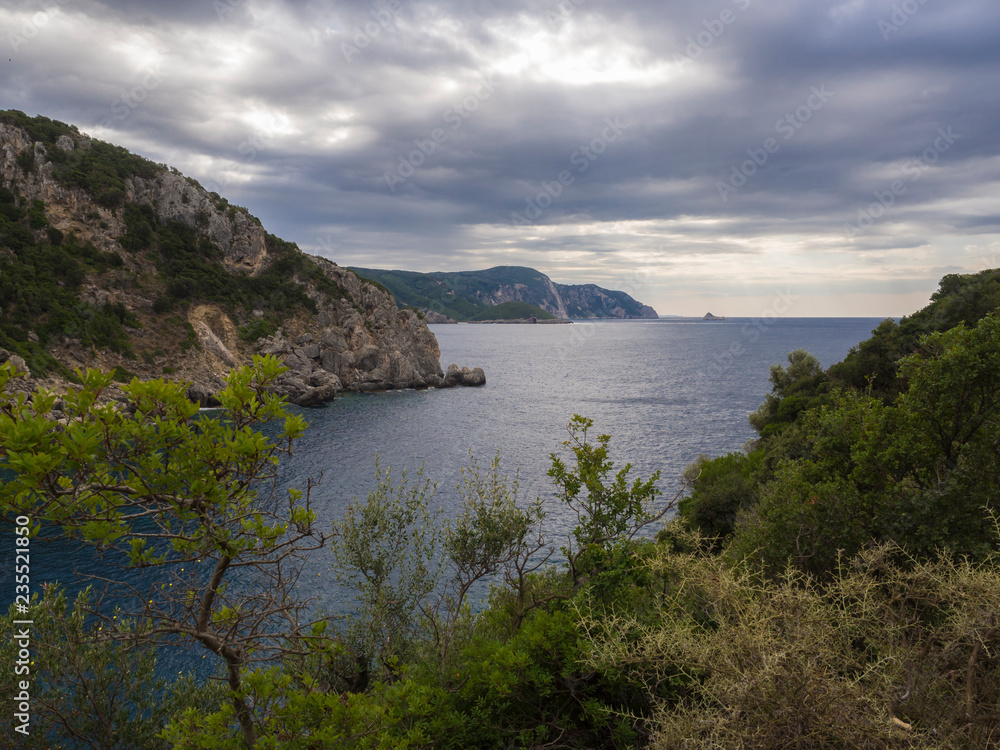 View on cllifs, trees and green hill at Paleokastritsa bay, summer cloudy sky, Corfu, Kerkyra, Greece