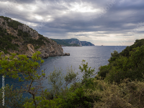 View on cllifs, trees and green hill at Paleokastritsa bay, summer cloudy sky, Corfu, Kerkyra, Greece