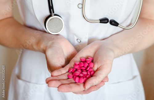 Doctor with stethoscope keeps a heap of pink pills close up