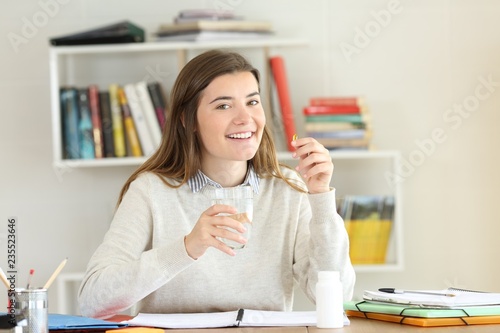Photography Happy student holding a vitamin pill on a desk