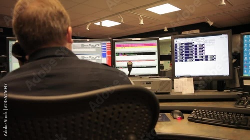 Man answering the phone in front of computer screens in a dolly shot. Emergency 911 call center 