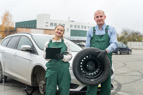 Two mechanics with tyre and clipboard near car © RomanR