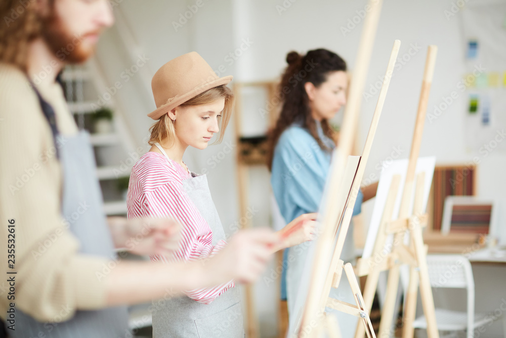 Fototapeta premium Young student of faculty of arts and her groupmates painting at lesson or course