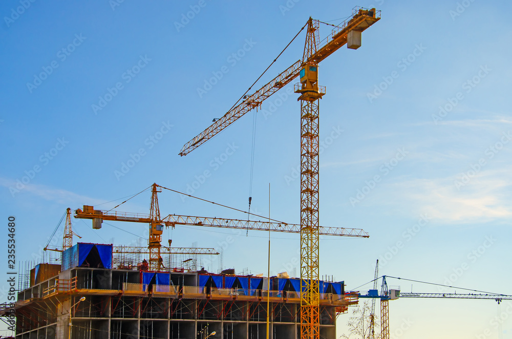 Building of a residential house, working cranes on a background of blue sky.