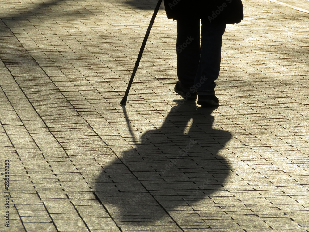 Silhouette of man walking with a cane, long shadow on pavement