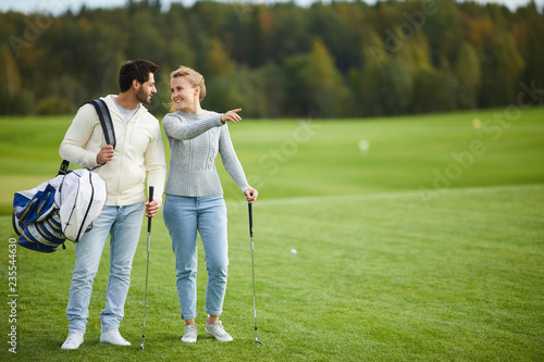 Young woman showing her boyfriend nice place for playing golf while both standing on large green field