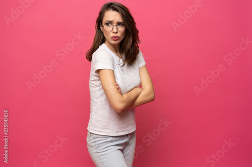 Portrait of an upset young casual girl standing with arms folded isolated over pink background.