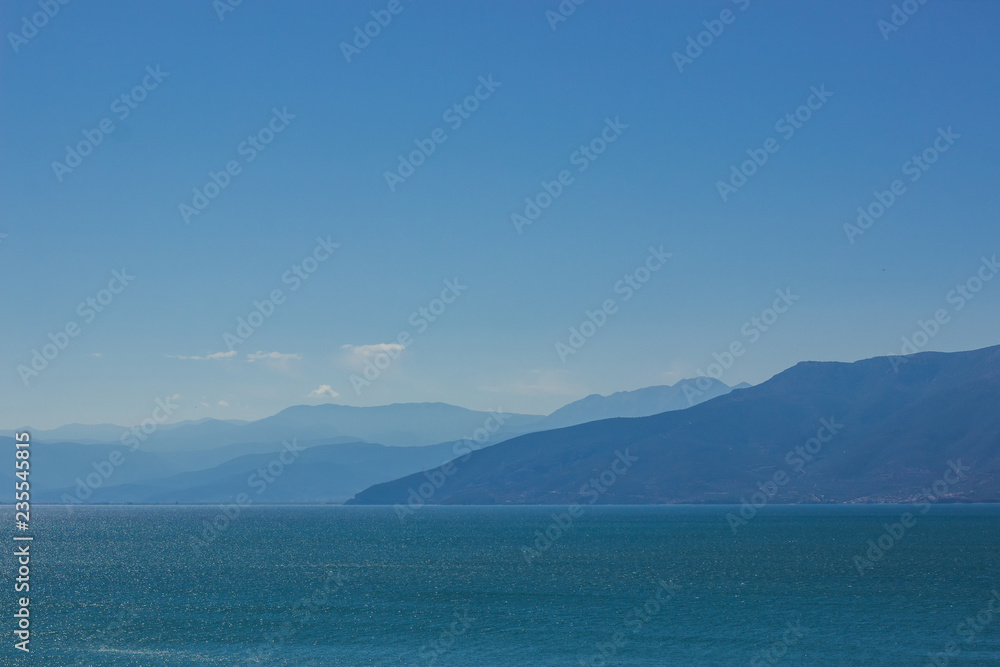 abstract wallpaper landscape of mountain ridge horizon silhouette and sea calm water surface in clear morning foggy weather time, copy space 