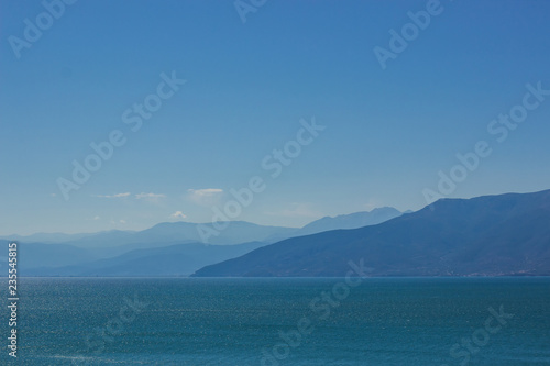 abstract wallpaper landscape of mountain ridge horizon silhouette and sea calm water surface in clear morning foggy weather time, copy space 