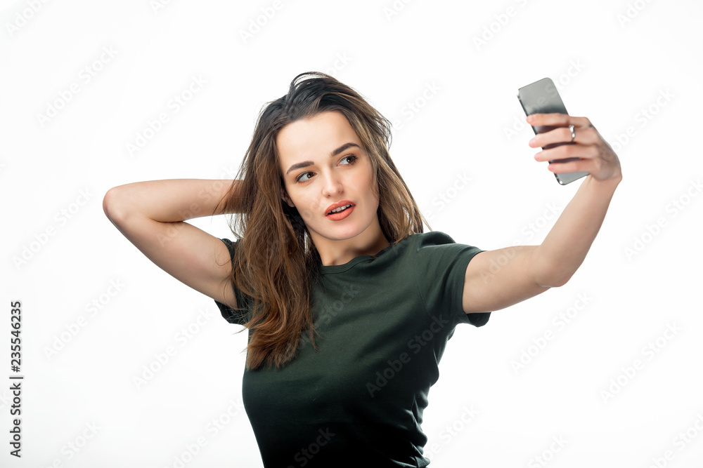 Beautiful girl taking selfie on white studio background. Long-haired young  female takes a selfie on her smartphone. Stock Photo | Adobe Stock