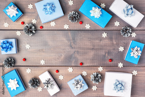 Small blue and white boxes with bows, red berries, silver cones and snowflakes, arranged in a circle. Christmas composition with copy space on wooden background. Festive layout.