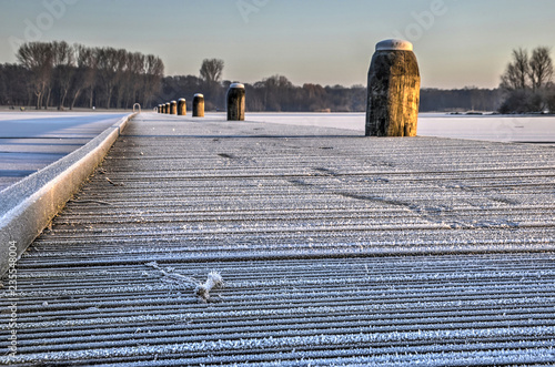 Low angle view of a wooden walkbridge across  lake Kralingse Plas in Rotterdam, The Netherlands covered with hoarfrost on a sunny day in winter photo