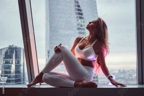 Beautiful girl sitting on a window sill in a skyscraper apartment.