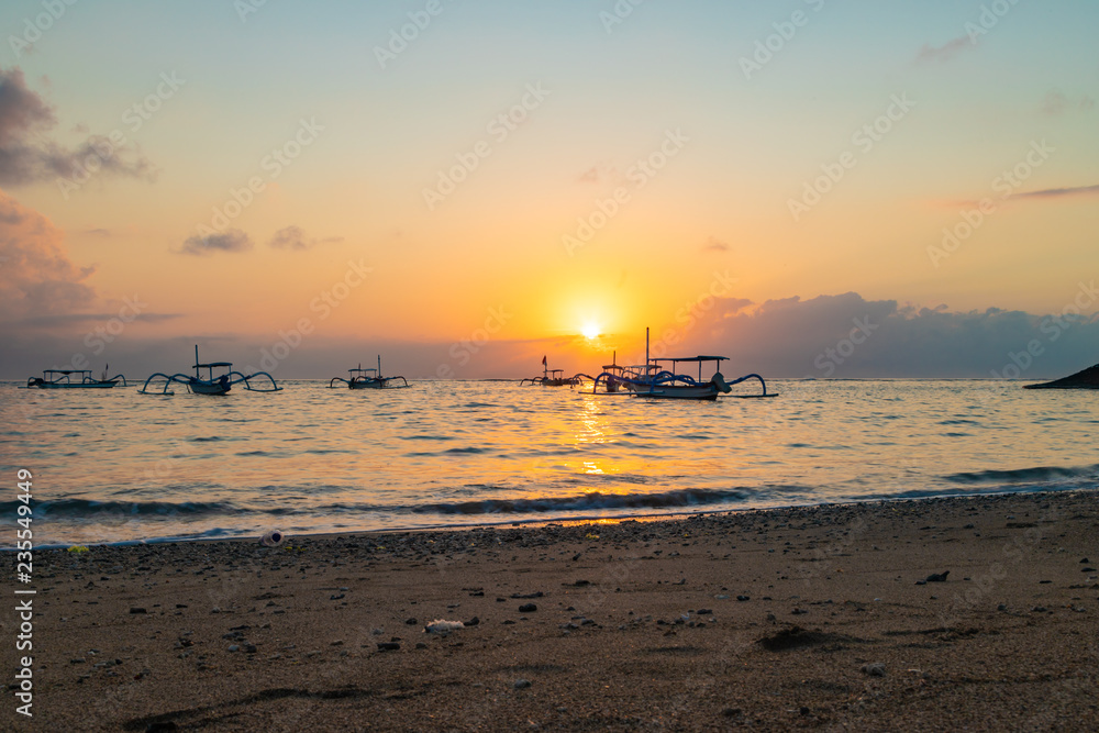 Beautiful sunrise at Sanur Beach, Bali. Traditional fishing boat on seashore at colorful sunrise. Indonesia.