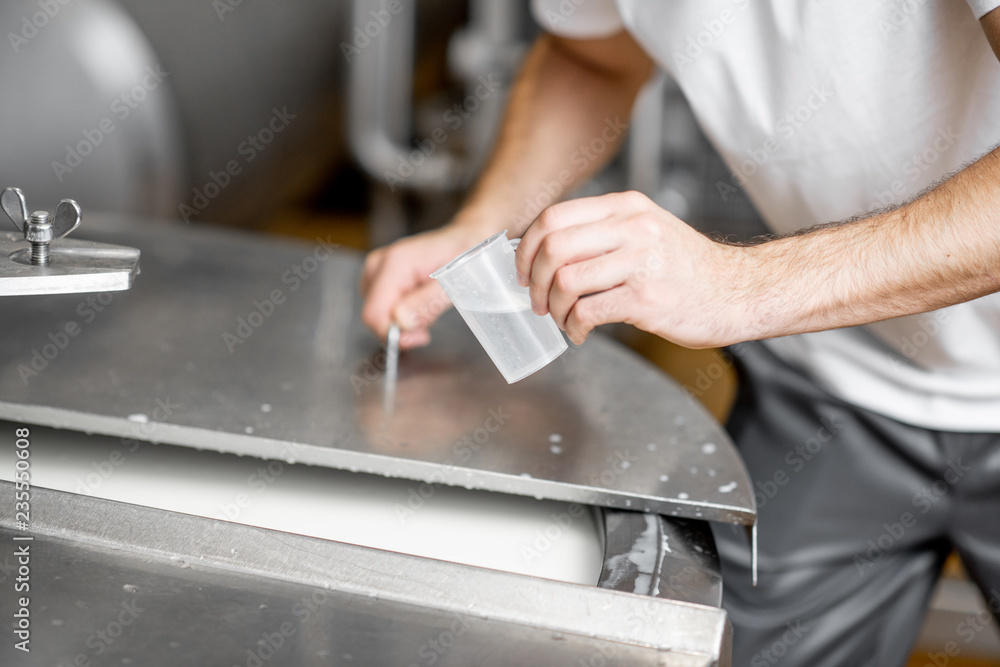 Worker adding supplements during the milk fermentation process in the stainless tank at the cheese manufacturing. Close-up view with no face