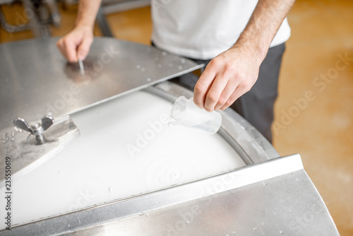 Фотография Worker adding supplements during the milk fermentation process in the stainless tank at the cheese manufacturing