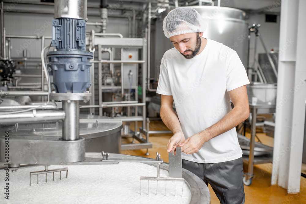 Man mixing milk in the stainless tank during the fermentation process at the cheese manufacturing Man mixing milk in the stainless tank during the fermentation process at the cheese manufacturing
