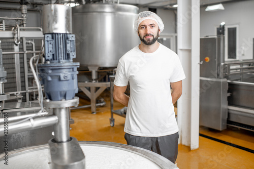 Portrait of a handsome worker in uniform near the stainless tank full with fermenting milk at the cheese manufacturing