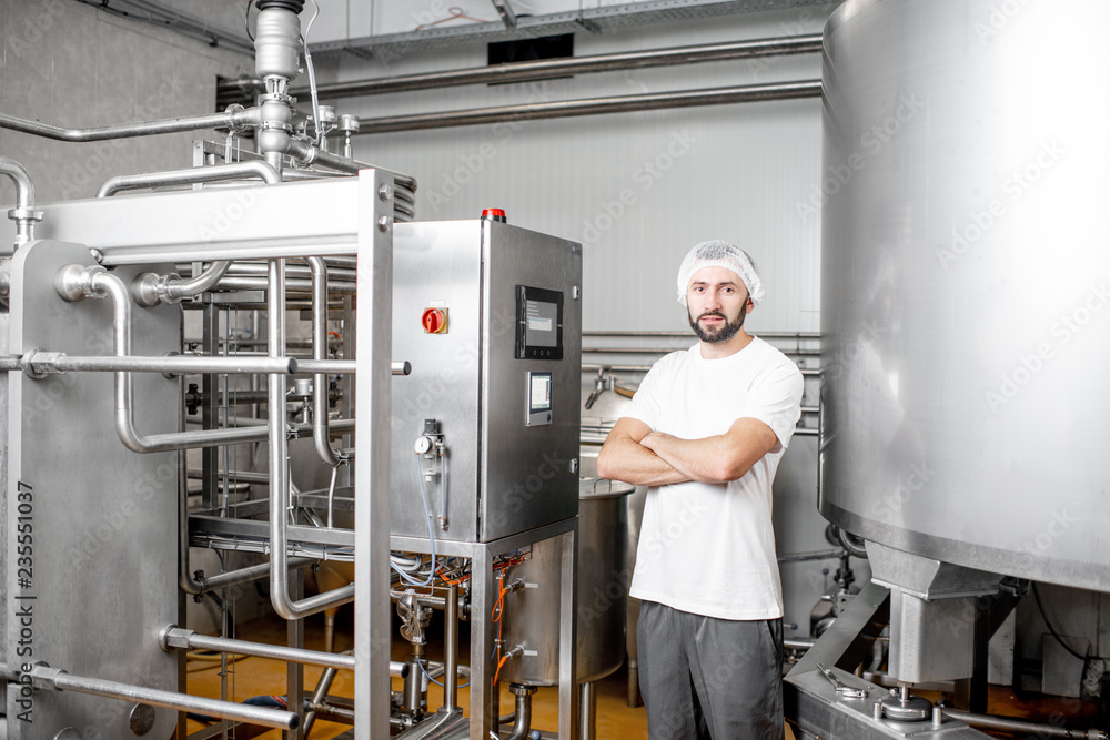 Portrait of a handsome worker operating pasteurizer using the control panel at the cheese or milk manufacturing Portrait of a handsome worker operating pasteurizer using the control panel at the cheese or milk manufacturing
