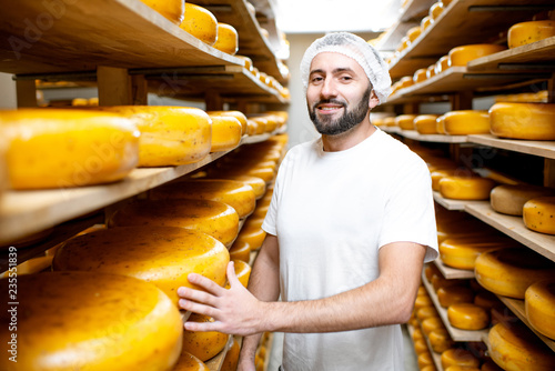 Cheese maker at the storage with shelves full of cheese wheels during the aging process photo