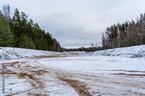 Car Tire Marks on an Empty Field Covered With Snow  Wood in the Background - Cloudy Day