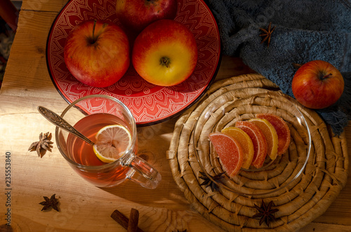 Apples in a ceramic red plate, a glass of mulled wine, sweets on a wooden table.