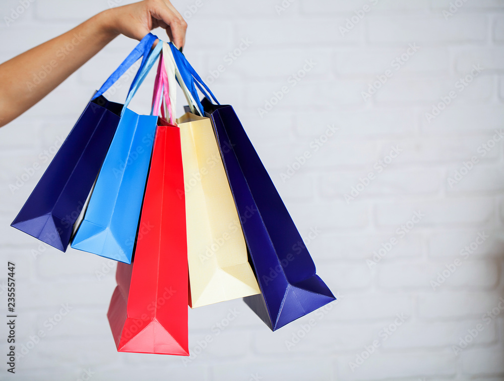 Shopping. Closeup of woman holding color paper shopping bag on white wall background